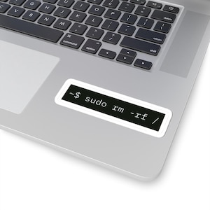 Puede incluir: Una pegatina blanca con un fondo rectangular negro, con el texto "~$ sudo rm -rf /". La pegatina está colocada en un portátil plateado, con el teclado visible.
