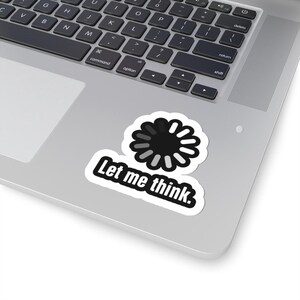 May include: A white sticker with the text "Let me think." in a black, bold font. Above the text is a black and white loading symbol. The sticker is on a silver laptop.
