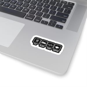 May include: A white sticker with black icons and text reading "EAT SLEEP CODE COFFEE" is placed on a laptop. The icons include a fork and knife, a bed, code brackets, and a coffee cup. The laptop keyboard is visible.