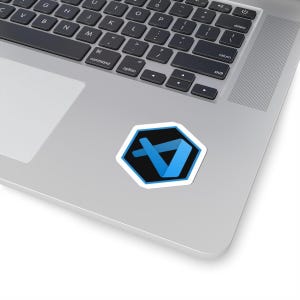 Op de afbeelding: Een sticker met een blauw en zwart logo met een witte rand, op een laptop. Het logo is een gestileerde blauwe "A" in een zwarte zeshoek. Het toetsenbord van de laptop is zichtbaar.