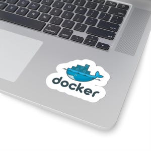 Peut inclure: Un autocollant blanc avec le mot "docker" en gras. Au-dessus du texte se trouve un graphique de baleine bleue avec un nuage et un design de conteneur. L'autocollant est sur un ordinateur portable.