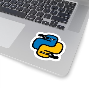 Może przedstawiać: Naklejka z logo języka programowania Python w kolorze niebieskim i żółtym, w pikselowanych okularach przeciwsłonecznych. Naklejka znajduje się na laptopie, z widoczną klawiaturą.