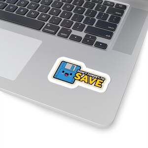 Puede incluir: Una pegatina con un disquete azul con una cara sonriente y el texto "DON'T FORGET TO SAVE" en amarillo y negro. La pegatina está sobre un portátil.