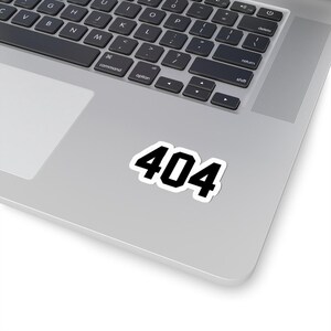 Può includere: Un adesivo bianco con il numero "404" in grassetto nero. L'adesivo è su un laptop argentato, vicino alla tastiera. La tastiera del laptop è nera.