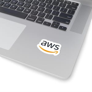 May include: A white sticker with the word "aws" in black, above an orange arrow. The sticker is on a silver laptop. The laptop keyboard is visible in the background.