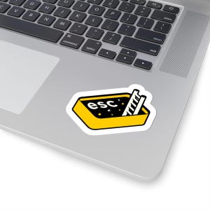 May include: A sticker showing a yellow rectangle with the word "esc" and a ladder inside. The background is black with white stars. The sticker is on a laptop.