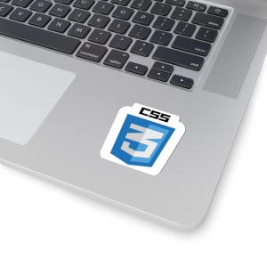 Op de afbeelding: Een witte sticker met een blauw en wit CSS3-logo, met de tekst "CSS" in zwart. De sticker is geplaatst op een zilveren laptop.