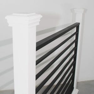 May include: A section of a modern railing with black horizontal bars and white posts. The posts have a decorative top. The railing is designed for safety and adds a contemporary aesthetic to any space.