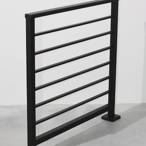 May include: Black metal railing with horizontal bars. The railing has a rectangular top and bottom, and is designed for safety and support. The minimalist design is suitable for both indoor and outdoor use.