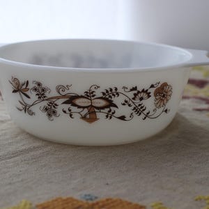 Puede incluir: Bol ovalado blanco con diseño floral marrón. El cuenco tiene dos asas y un patrón decorativo de flores y hojas. Un artículo de cocina vintage.