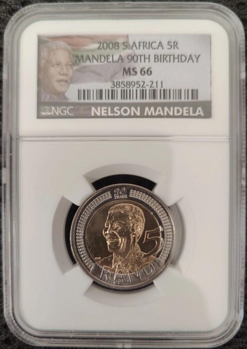 Op de afbeelding: Een Zuid-Afrikaanse 5 Rand munt uit 2008 ter herdenking van de 90e verjaardag van Nelson Mandela, beoordeeld als MS 66 door NGC. De munt toont een portret van Mandela, het cijfer 5 en de tekst 90 YEARS en RAND, verpakt in een doorzichtige houder.