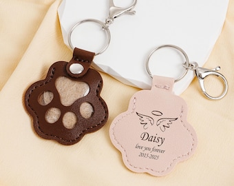 May include: Two leather paw-shaped keychains. One is brown with a silver key ring and clasp. The other is pink with the name "Daisy", angel wings, and the text "love you forever 2015-2025".