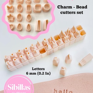 May include: A set of light pink charm and bead cutters, including various shapes and letters. The letters are 6 mm (0.2 in) tall. The word "hello" is stamped into a pink surface. The text "Charm - Bead cutters set" is visible.