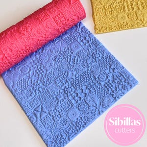 May include: A close-up of three textured rolling pins and a sheet with a repeating pattern. The rolling pins are red, blue, and yellow. The blue sheet has a repeating pattern of squares with various designs. The image has the text "Sibillas cutters".