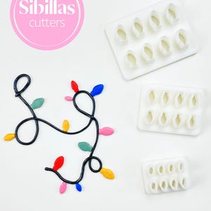 May include: Image features Christmas light-shaped cookie cutters and a decorative string of lights. The cutters are white plastic, and the lights are in various colors. The Sibillas Cutters logo is in a pink circle.