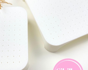 May include: Two white, rectangular cutters with rounded corners and small, evenly spaced holes. The cutters have a slightly raised edge and are set against a white background. The image includes a pink circle with the text "Sibillas cutters".