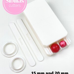May include: A white bead making kit with the text "Sibillas cutters". The kit includes two white bead rollers, two white tools, and a white container holding a red and a pink bead. The text "15 mm and 20 mm BEADS" is also visible.