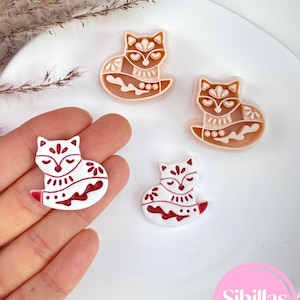 Könnte beinhalten: Vier fuchsförmige Ausstecher. Zwei sind weiß mit roten Details, und zwei sind braun mit beigen Details. Die Fuchsmotive haben florale und geometrische Muster. Die Ausstecher befinden sich auf einem weißen Teller. Der Text "Sibillas cutters" ist ebenfalls vorhanden.