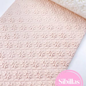 May include: A roll of pink fondant with a repeating floral pattern, partially unrolled to reveal a white fondant with the same design. The image includes the text "Sibillas cutters" in a pink circle.