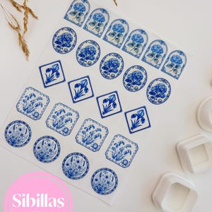 Op de afbeelding: Een vel wit transferpapier met een verzameling blauw-witte bloemenillustraties in verschillende vormen, waaronder cirkels, vierkanten en bogen. De ontwerpen tonen hortensia's en andere botanische motieven. Drie witte plastic uitsteekvormen zijn zichtbaar.