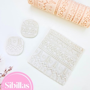 Può includere: Una collezione di strumenti per la cottura a tema invernale. Include un mattarello decorato, due piccoli tagliapasta ovali e un tagliapasta rettangolare, tutti di colore beige chiaro. I tagliapasta e il mattarello presentano intricati disegni in rilievo.