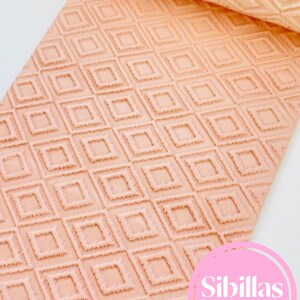 May include: A peach-colored rolling pin with a repeating diamond pattern. The rolling pin is partially rolled out, revealing the textured design. The text "Sibillas cutters" is in a pink circle in the lower right corner.