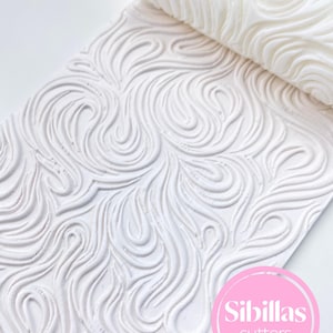 Könnte beinhalten: Weißer Nudelholz und strukturierte Matte mit einem Wirbelmuster. Das Nudelholz ist teilweise ausgerollt und zeigt das detaillierte Design. Matte und Nudelholz sind beide weiß. Das Bild enthält einen rosa Kreis mit dem Text "Sibillas cutters".