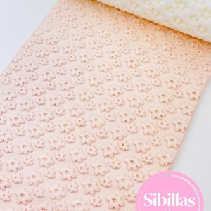 Può includere: Un mattarello rosa chiaro e un foglio di materiale rosa chiaro, entrambi in rilievo con un motivo floreale ripetuto. Il mattarello è bianco. L'immagine include il testo "Sibillas cutters" in un cerchio rosa.