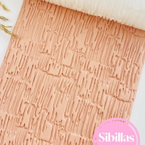 May include: A textured, light peach-colored rolling pin with a white roller. The rolling pin is designed to create a textured pattern on fondant or dough. The image also includes the text "Sibillas cutters" in a pink circle.
