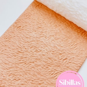 May include: A roll of textured, peach-coloured material with a wave-like pattern. A white roll is partially visible at the top. The image includes a pink circle with the text "Sibillas cutters".
