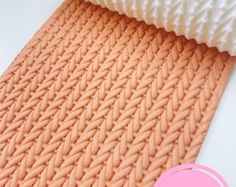May include: A white textured rolling pin is shown partially rolled over a peach-colored fondant sheet, creating a knitted pattern. The image features a close-up view of the textured surface, ideal for cake decorating. The Sibillas Cutters logo is visible.