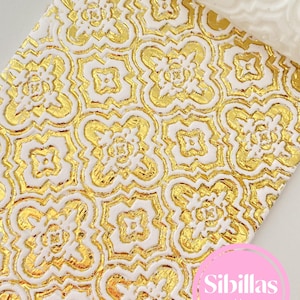 May include: Close-up of a white and gold patterned rolling pin. The pattern is a repeating gold floral design on a white background. The text "Sibillas cutters" is in a pink circle in the lower right corner.
