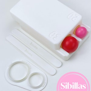 May include: A white plastic cake decorating kit with a container holding a red and pink sphere, two white strips marked "3mm", and two circle cutters. The kit includes the text "Sibillas cutters" in a pink circle.