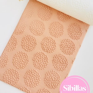 Puede incluir: Un rodillo de amasar de color melocotón claro con un patrón floral extendido sobre una superficie a juego de color melocotón. El rodillo es blanco con el mismo diseño floral. El texto "Sibillas cutters" está en un círculo rosa.