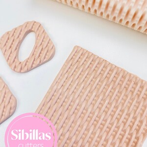 May include: A selection of light peach-coloured baking tools, including a textured rolling pin, a square cutter, and a square with a hole cutter. The tools have a woven pattern design. The image includes a pink logo that says "Sibillas cutters".