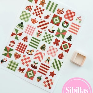 May include: A rectangular sheet of paper featuring a grid of small square Christmas-themed illustrations in red, green, and white, including gingerbread men, trees, and patterns. A single light-colored square plastic cutter sits nearby.