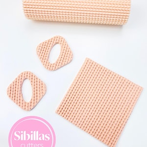 May include: Peach-coloured baking tools are displayed on a white surface. The set includes a textured rolling pin, two square cutters with oval centres, and a textured square mat. A pink circle with the text "Sibillas cutters" is also visible.
