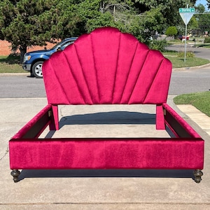 Puede incluir: Una cabecera de terciopelo carmesí con un diseño de concha. La cabecera está unida a un marco de cama a juego con patas de madera oscura.