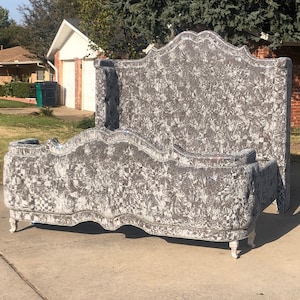 Puede incluir: Una cabecera y un piecero tapizados en gris con un diseño capitoné. La cabecera es alta y tiene una parte superior curva. El piecero es más bajo y tiene una parte inferior curva. El marco de la cama está hecho de madera y tiene un acabado blanco.