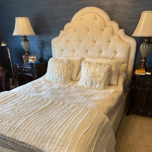 May include: A white upholstered bed frame with a tufted headboard and a white quilted bedspread. The headboard has a decorative arched top with crystal-like embellishments.