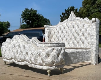 May include: A white tufted headboard with a decorative crown detail. The headboard is part of a large, white tufted bed frame with a matching footboard.