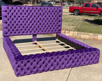 Puede incluir: Una cabecera y un piecero acolchados de color morado con un marco de listones de madera. La cama está tapizada en un tejido de terciopelo suave.