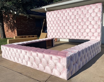 Puede incluir: Un gran marco de cama capitoné de color rosa con cabecero y piecero. El marco de la cama está hecho de una tela suave y mullida y tiene un diseño capitoné.
