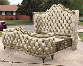 May include: A tufted, upholstered bed frame in a light gold color. The headboard is tall and rectangular, with a curved footboard. The fabric has a velvet-like texture, and the frame sits on small, dark legs.