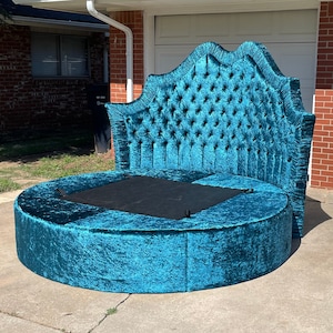 Puede incluir: Una cama redonda de color azul turquesa con un cabecero capitoné y un colchón negro. La cama está tapizada en un tejido de terciopelo suave y mullido.