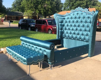May include: A teal upholstered bed frame and matching bench. The bed features a tall, button-tufted headboard with crystal accents. The bench has a similar design with clear acrylic legs. The bed frame is designed for a standard mattress.