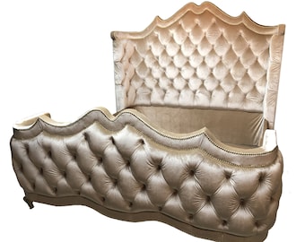 May include: A large, tufted, beige velvet headboard with a curved, scalloped design. The headboard is upholstered in a soft, luxurious fabric and features a tufted design with gold buttons.