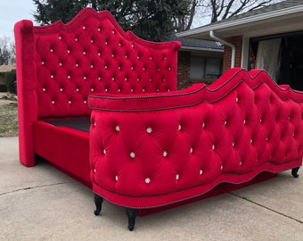 Puede incluir: Una cabecera tapizada de terciopelo rojo con un diseño curvo y botones de cristal. La cabecera está unida a un marco de cama de terciopelo rojo a juego con ribetes negros y patas negras.