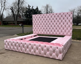Puede incluir: Un gran marco de cama de color rosa capitoné con cabecero y piecero. El marco de la cama está tapizado en un tejido suave de terciopelo y tiene un diseño capitoné.