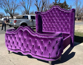 May include: A large, purple velvet bed frame with a tufted headboard and footboard. The bed frame has a decorative, ornate design and silver-colored legs.